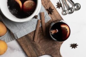 Warm mulled wine with lemon slices, star anise, and cinnamon sticks on a wooden board.