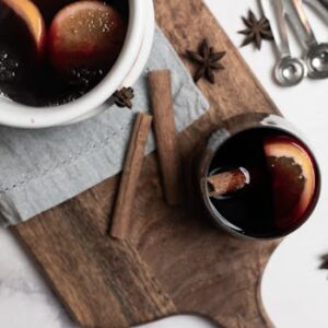 Warm mulled wine with lemon slices, star anise, and cinnamon sticks on a wooden board.